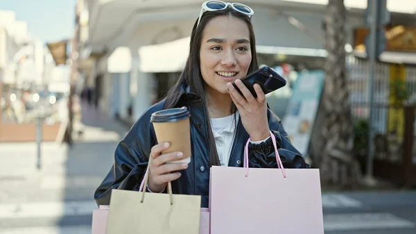 コーヒーショップのテラスで買い物袋やコーヒーを持ってスマートフォンで音声メッセージを送信若い美しいヒスパニック女性 — ストック写真