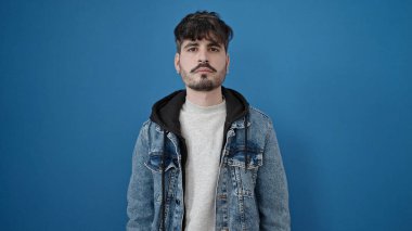 Soyutlanmış mavi arka planda ciddi bir ifadeyle duran İspanyol genç adam.