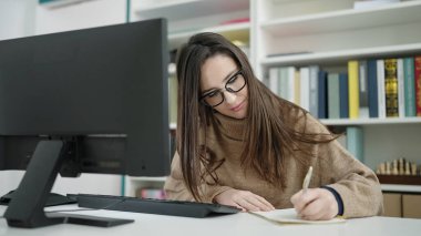 Güzel İspanyol kız öğrenci kütüphanede defter üzerine bilgisayar kullanıyor.