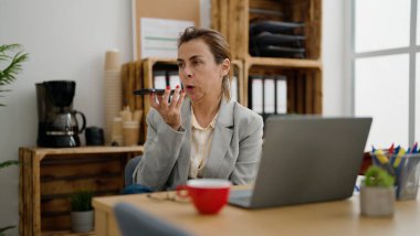 Orta yaşlı İspanyol iş kadını ofisteki akıllı telefondan konuşuyor.