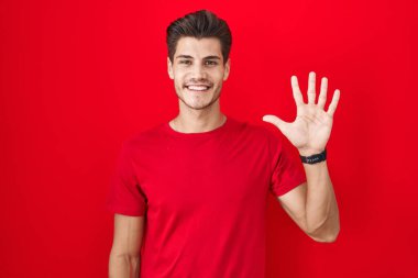 Young hispanic man standing over red background showing and pointing up with fingers number five while smiling confident and happy. 