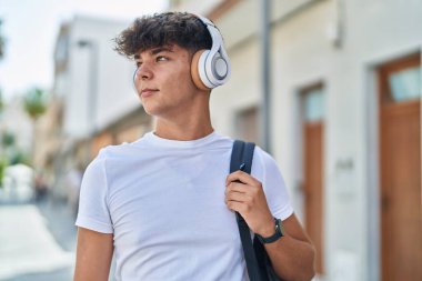 Young hispanic teenager student listening to music with relaxed expression at street