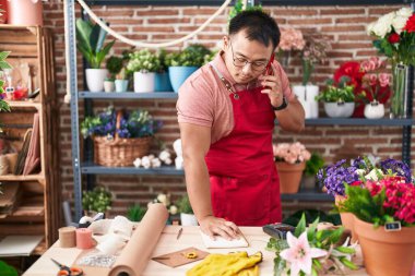 Genç Çinli çiçekçi çiçekçi çiçekçide defterde akıllı telefondan konuşuyor.