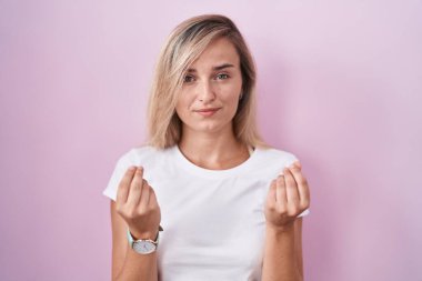 Pembe arka planda duran genç sarışın kadın. Elleriyle para hareketi yapıyor. Maaş istiyor. 