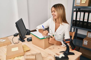 Young hispanic woman ecommerce business worker writing on document at office