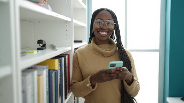 African woman smiling using smartphone at library university