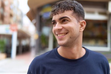 Young hispanic man smiling confident looking to the side at street