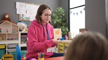 Young blonde woman preschool teacher having vocabulary lesson at kindergarten