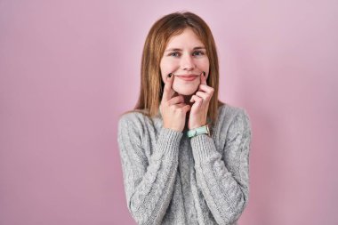 Pembe arka planda duran güzel kadın ağzı açık gülümsüyor, parmakları işaret ediyor ve zorla neşeli bir gülümseme sergiliyor. 