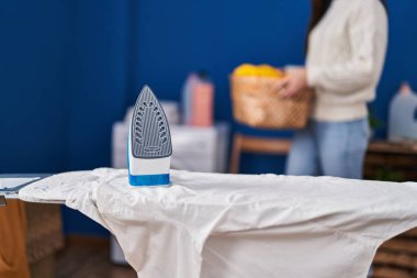 Çamaşır odasında çamaşır sepetini tutan genç bir kadın.