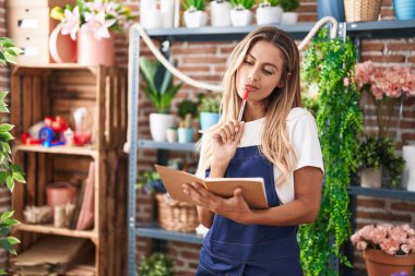 Çiçekçide şüpheli bir ifadeyle not defterine yazan sarışın kadın.