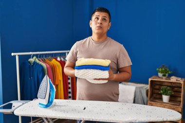 İspanyol genç adam ütüledikten sonra çamaşırları katladı. Gülümsedi ve başka tarafa baktı.. 