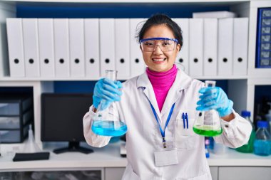 Bilim adamlarının laboratuvarında çalışan Asyalı genç bir kadın yüzünde mutlu ve havalı bir gülümsemeyle gülümsüyor. diş gösterme. 