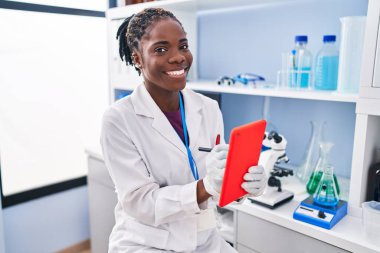 Laboratuvarda dokunmatik ped kullanan Afrikalı Amerikalı kadın bilim adamı üniforması giyiyor.