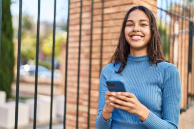 Genç Afro-Amerikalı kadın sokakta akıllı telefon kullanarak gülümsüyor.