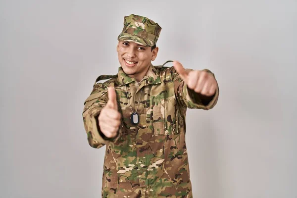 カモフラージュ軍の制服を着た若いアラブ人男性は 手で積極的なジェスチャーを行うことを承認し 親指を笑顔と成功のために幸せ 勝者のジェスチャー — ストック写真