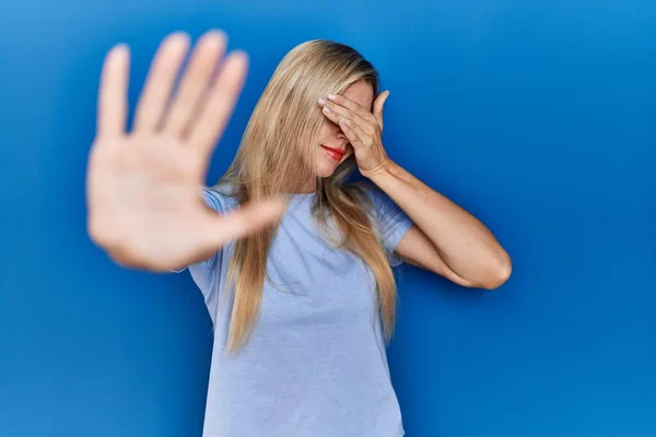 Mooie Blonde Vrouw Draagt Casual Shirt Blauwe Achtergrond Bedekken Ogen — Stockfoto