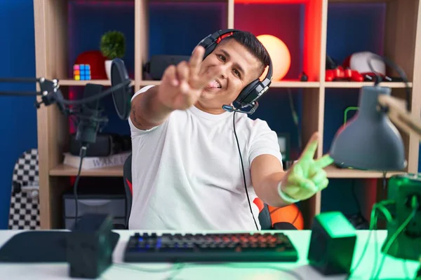 Молодой Латиноамериканец Играющий Видеоигры Улыбаясь Языком Показывает Пальцы Обеих Рук — стоковое фото