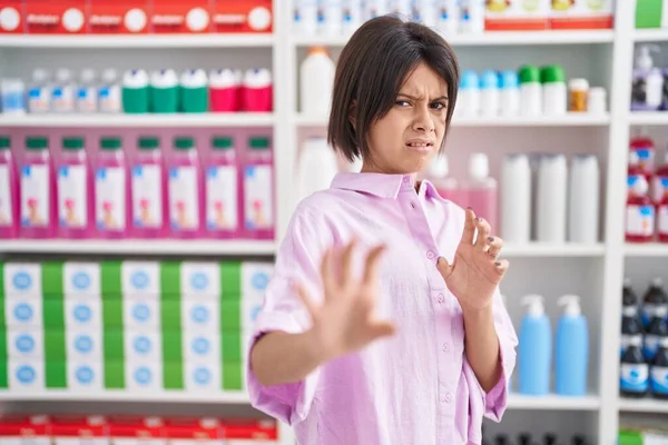Young girl at pharmacy drugstore disgusted expression, displeased and fearful doing disgust face because aversion reaction. with hands raised