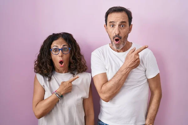 Middelbare Leeftijd Hispanic Paar Samen Roze Achtergrond Verrast Wijzend Met — Stockfoto