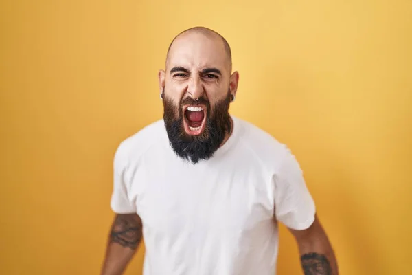 ひげと入れ墨を持つ若いヒスパニック系の男は 黄色の背景怒っていると怒りを叫び 怒りで叫んで立っている 怒りと攻撃的な考え方 — ストック写真