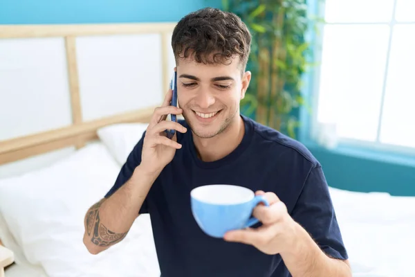 stock image Young hispanic man talking on smartphone drinking coffee at bedroom