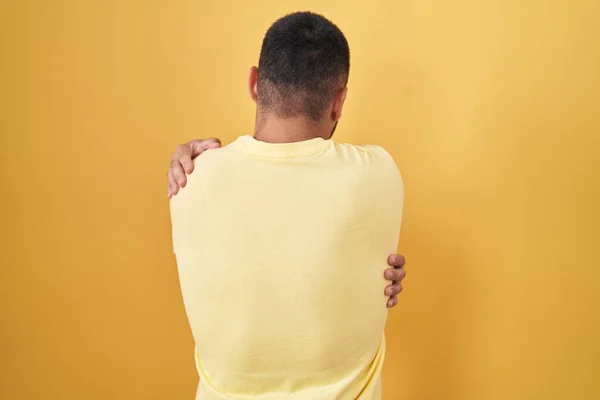 Νεαρός Ισπανός Στέκεται Πάνω Από Κίτρινο Φόντο Αγκαλιάζοντας Τον Εαυτό — Φωτογραφία Αρχείου