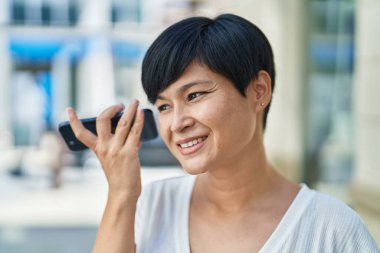 Orta yaşlı Çinli kadın gülümsüyor. Caddedeki akıllı telefondan kendine güvenen sesli mesaj dinliyor.