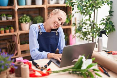 Çiçekçide dizüstü bilgisayarla konuşan sarışın bir çiçekçi.