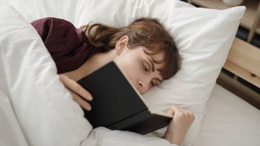 Young caucasian woman reading a book in the bed at bedroom