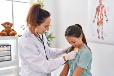 Woman and girl doctor and patient auscultating chest at clinic