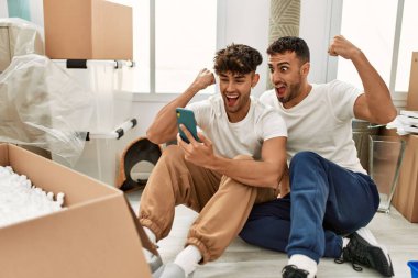 İki İspanyol erkek yeni evinde akıllı telefon kullanarak gülümsüyor.