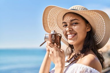 Genç Afro-Amerikan kadın turist deniz kenarında kamera kullanarak gülümsüyor.