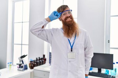 Laboratuvarda duran, bilim adamı üniforması giyen genç kızıl saçlı adam.