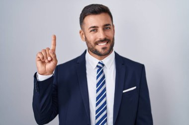 Yakışıklı İspanyol takım elbiseli ve kravatlı bir numaralı parmağını gösterip işaret ederken kendinden emin ve mutlu gülümsüyor.. 