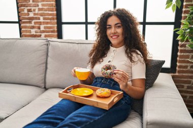 Genç, güzel, İspanyol bir kadın kahvaltısını evde, koltukta yapıyor.