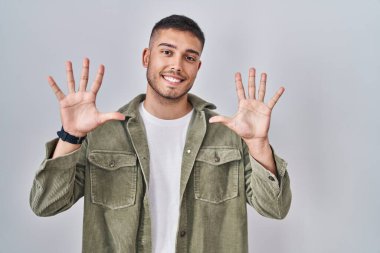 İzole edilmiş arka planda duran genç İspanyol adam on numarayı gösterip işaret ederken kendinden emin ve mutlu bir şekilde gülümsüyor.. 