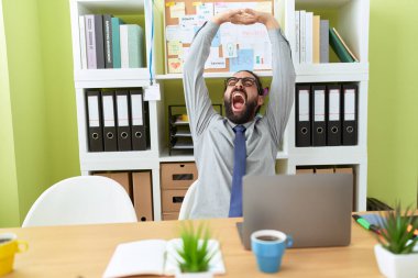 Genç İspanyol iş adamı kollarını açıp ofiste esniyor.