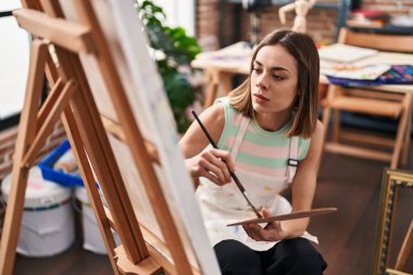 Young beautiful hispanic woman artist drawing with relaxed expression at art studio