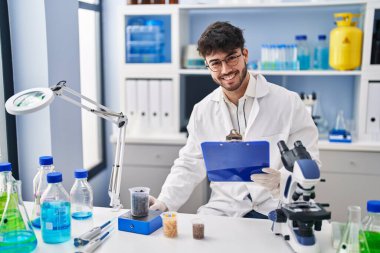 Young hispanic man scientist weighing sample reading document at laboratory