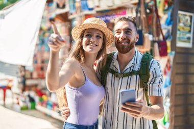 Erkek ve kadın turist çift, markette akıllı telefon kullanarak gülümsüyor.