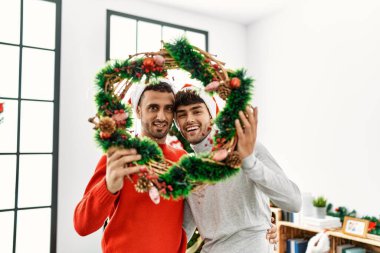 İki İspanyol erkek, Noel süslerini evde tutarak birbirlerine sarılıyorlar.