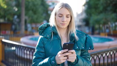 Young blonde woman using smartphone at park