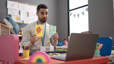 Young hispanic man working as teacher teaching online words lesson at kindergarten