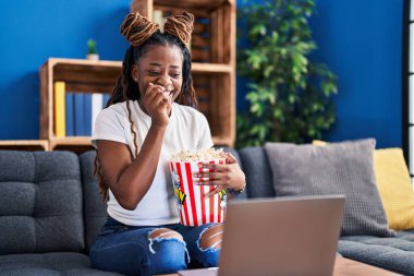 Afro-Amerikalı kadın evde kanepede oturmuş film izliyor.