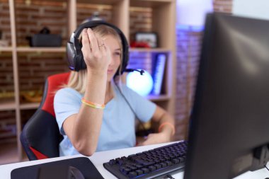 Genç beyaz kadın video oyunları oynuyor kulaklık takıyor italyan jestleri yapıyor ve parmakları kendinden emin. 