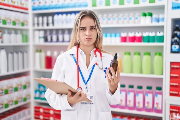 在药店工作的金发碧眼的年轻妇女带着对瓶子的怀疑和紧张 因为问题皱着眉头 消极的人 — 图库照片