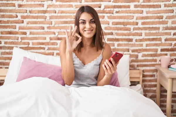 Молода Іспаномовна Жінка Використовуючи Смартфон Сидячи Ліжку Вдома Робить Знак — стокове фото