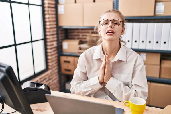 Young caucasian woman working at small business ecommerce using laptop begging and praying with hands together with hope expression on face very emotional and worried. begging.