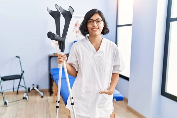 Young Latin Woman Wearing Physiotherapist Uniform Holding Crutches Physiotherapy Clinic — Stock Photo, Image